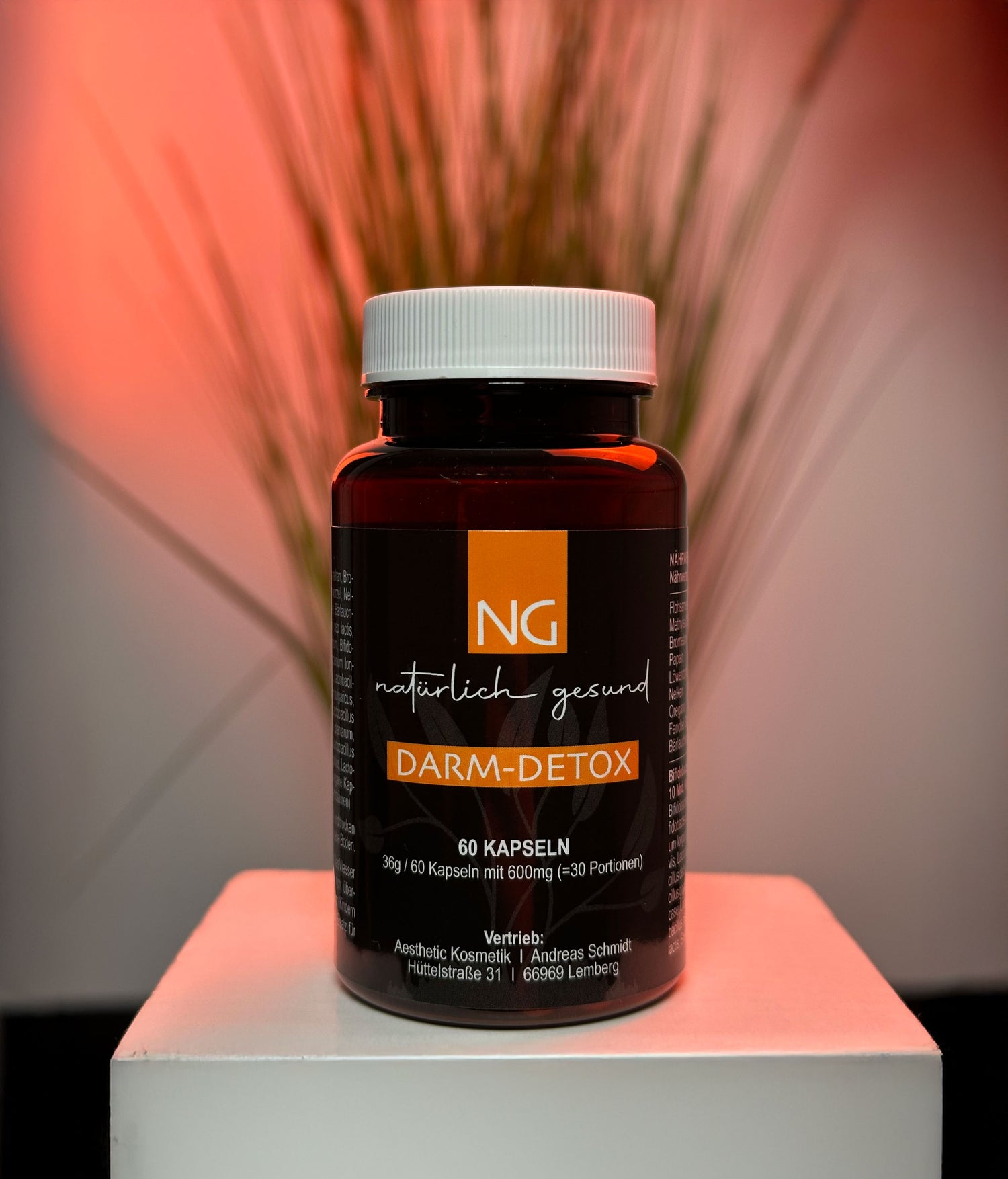 Auf einem weißen Tisch steht eine Produktdose mit der Aufschrift Darm-Detox. Sie wird orange Beleuchtet, im Hintergrund steht eine Pflanze
